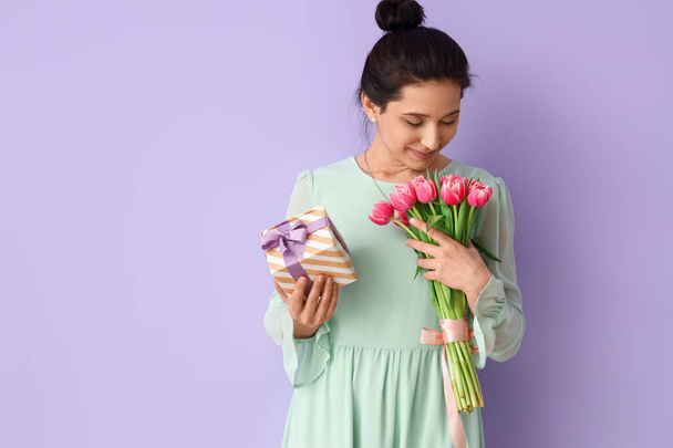 Femme avec cadeau et bouquet de fleurs sur fond de couleur - Photo, image