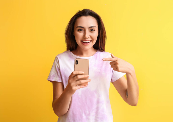 Femme souriante pointant vers le téléphone portable sur fond jaune. Concept de courrier électronique - Photo, image
