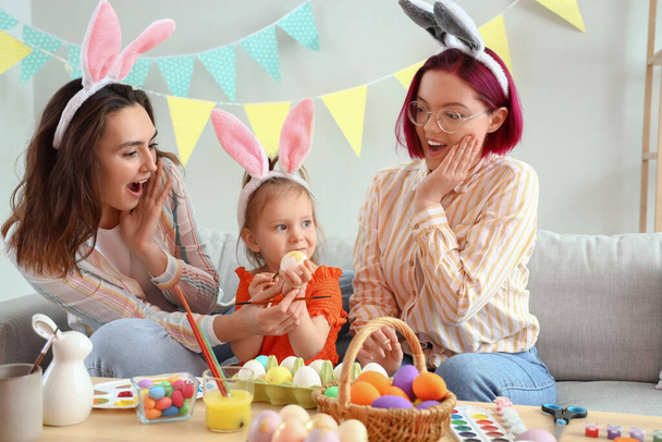 Young lesbian couple with little daughter painting Easter eggs at home - Photo, Image