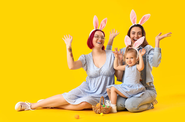 Счастливая лесбийская пара с маленькой дочерью и пасхальные яйца на цветном фоне - Фото, изображение