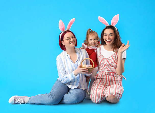 Feliz pareja lésbica con hija pequeña y huevos de Pascua sobre fondo de color - Foto, Imagen
