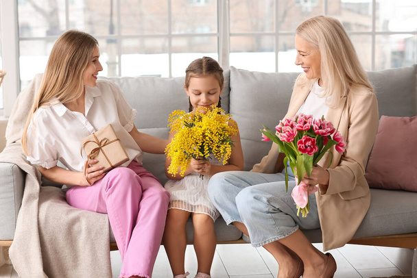 Giovane donna, sua figlia e sua madre con fiori a casa nella Giornata internazionale della donna - Foto, immagini