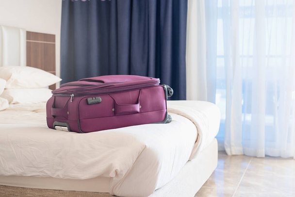 Διακοπές. μωβ βαλίτσα στο κρεβάτι στο δωμάτιο του ξενοδοχείου - Φωτογραφία, εικόνα
