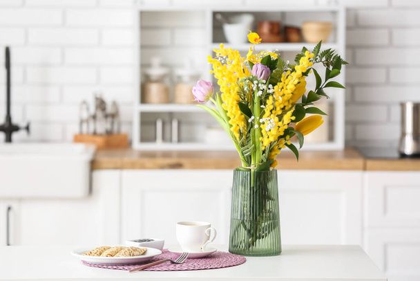 Piękne kwiaty, filiżanka kawy i talerz z naleśnikami na stole jadalnym w kuchni - Zdjęcie, obraz