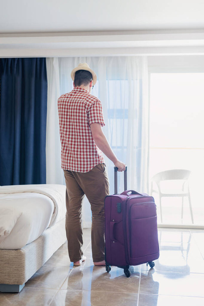 Wakacje. przystojny biały młody człowiek w letni kapelusz pakowanie jego walizka dla podróż - Zdjęcie, obraz