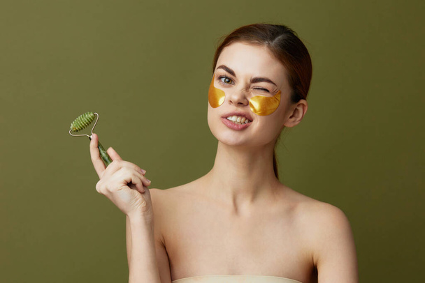 mujer bonita con masajeador facial y parches dorados en el primer plano de la cara Lifestyle. Foto de alta calidad - Foto, Imagen