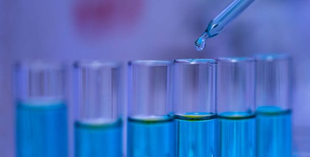 病院研究室での科学実験を分析するためにラック内のガラスウェア試験管ラインに青色の試薬溶剤溶液液サンプルをドロップ科学研究室のガラスドロッパーの閉鎖スタジオショット. - 写真・画像