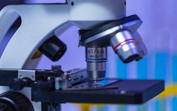 Detailní záběr lupy zvětšovací objektiv mikroskop umístění kamery na pracovním stole v nemocniční laboratoři plné skleněné vybavení zkumavky stojan Erlenmeyer baňka kádinka a počítačový monitor. - Fotografie, Obrázek