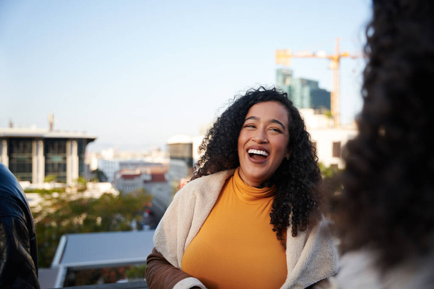 Multi-cultural young adult female laughing with friends at a rooftop party in the city, Good times, night life - Foto, afbeelding