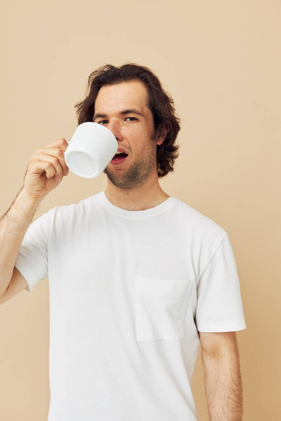 handsome man with a white mug in his hands emotions posing beige background - Foto, imagen