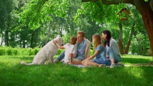 Młoda rodzina pieści labradora na pikniku. Szczęśliwi ludzie odpoczywają z psem na zewnątrz. - Materiał filmowy, wideo