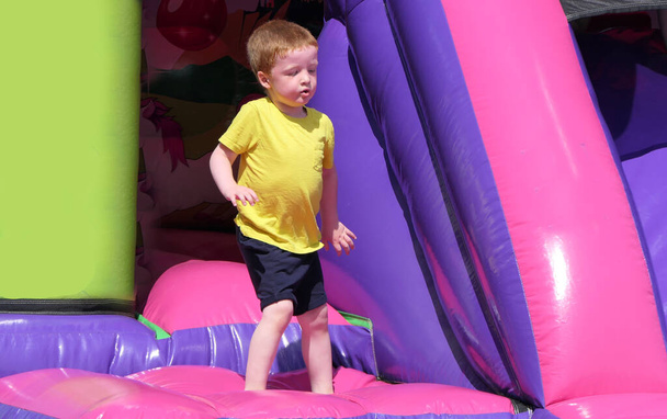 menino de cabeça vermelha se divertindo jogando em um castelo bouncy - Foto, Imagem