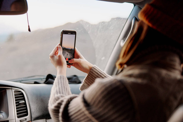 Nainen puhelin kädessään ottamassa kuvia luonnosta autossa. Laadukas kuva - Valokuva, kuva