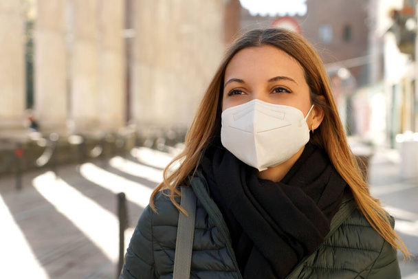 Mujer rubia joven con máscara médica protectora caminando por la ciudad con ropa de invierno - Foto, imagen