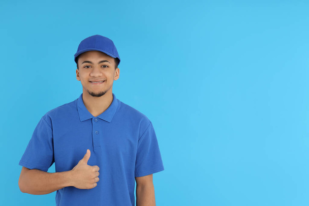 Young delivery man in cap on blue background - Zdjęcie, obraz