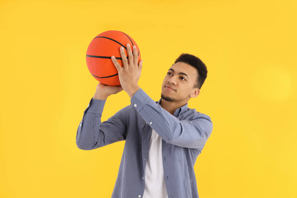 Young man with basketball ball on yellow background - Photo, Image