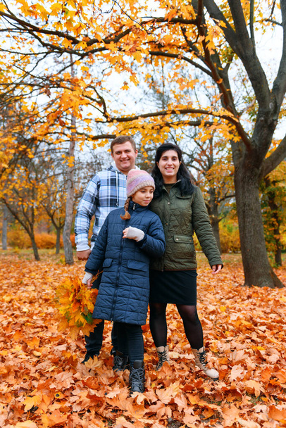 Porträt einer Familie mit Kindern in einem herbstlichen Stadtpark - glückliche Menschen posieren gemeinsam neben einem großen Baum, schöne Natur mit gelben Blättern als Hintergrund. - Foto, Bild