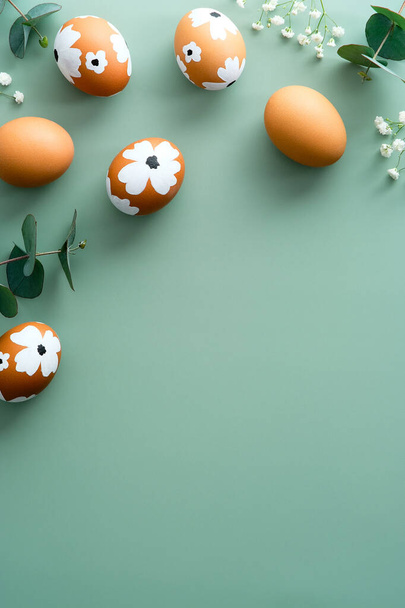 Happy Easter vertical banner design. Easter eggs decorated with flowers and eucalyptus leaves on pastel green background. Flat lay, top view. - Photo, image