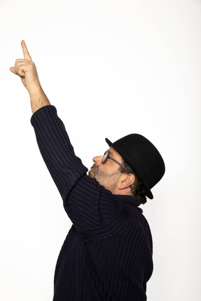 Man in profile points upward with his finger. He is wearing a blue sweater, jeans and a bowler hat. Isolated on white background - Foto, immagini