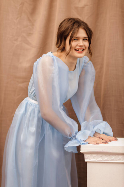 a girl in a blue dress leaning on a bedside table - Zdjęcie, obraz