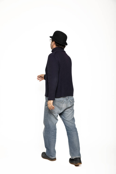Three-quarter man walks to the left. He is wearing a blue sweater, jeans and a bowler hat. Isolated on white background - Photo, Image