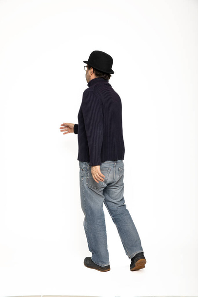 Three-quarter man walks to the left. He is wearing a blue sweater, jeans and a bowler hat. Isolated on white background - Foto, Imagen
