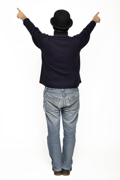 Man from behind rejoices with his arms up. He is wearing a blue sweater, jeans and a bowler hat. Isolated on white background - Photo, image