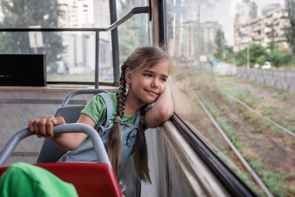 Young girl rides in empty tram and looks at the window dreamily, public transportation, city tramway - Photo, Image