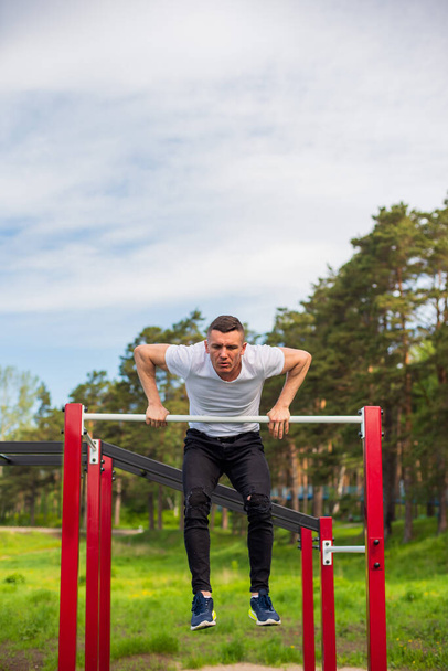 Caucasian man pulls himself up on a horizontal bar on a sports ground. - Фото, зображення