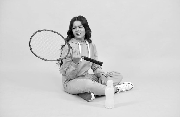 niño infeliz sentarse con raqueta botella de agua. niño con raqueta de tenis. adolescente chica yendo a beber agua - Foto, imagen