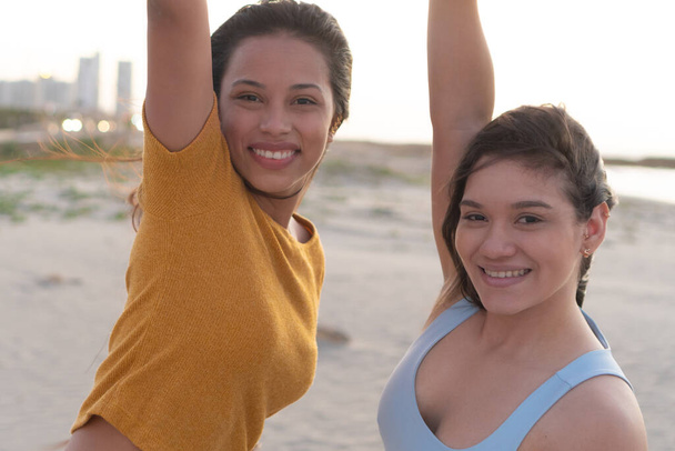 Two happy young friends standing with their hands raised near the beach - Foto, imagen