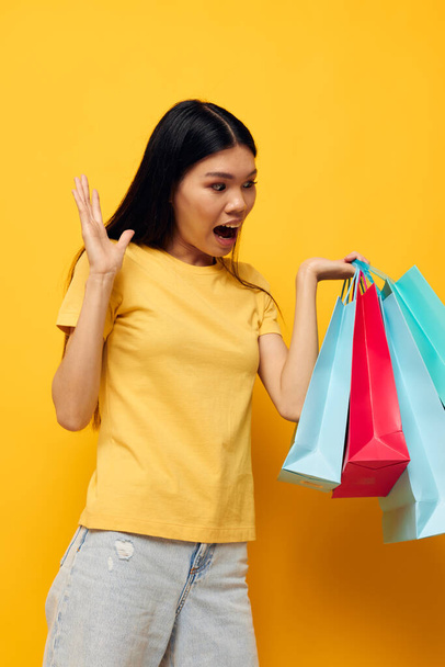 Portrait Asian beautiful young woman in a yellow T-shirt with multicolored shopping bags studio model unaltered - Foto, Imagem