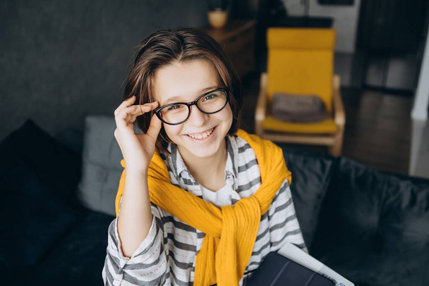 A teenage girl in glasses with dark hair wearing a yellow sweater laughs in the frame - Photo, Image