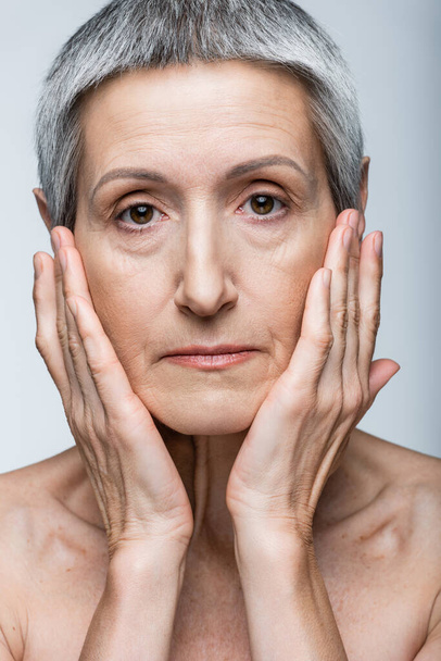 middle aged woman touching cheeks isolated on grey - Photo, image