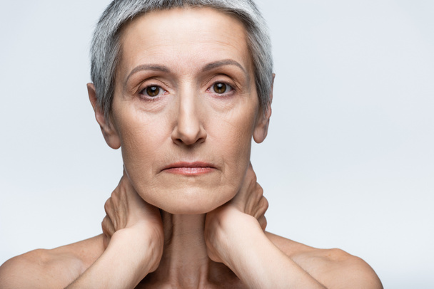 Frau mittleren Alters berührt Hals isoliert auf grau - Foto, Bild