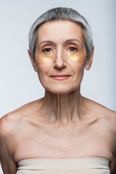 женщина средних лет в глазных повязках, смотрящая на камеру, изолированную на сером - Фото, изображение
