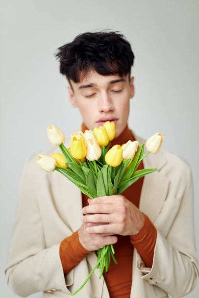 pretty man in white jacket with a bouquet of yellow flowers elegant style model studio - Photo, Image