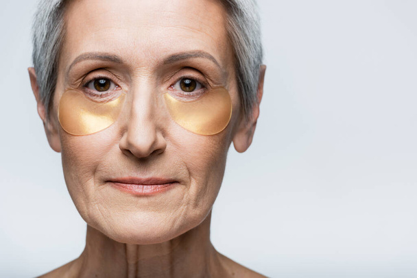 close up of middle aged woman in collagen eye patches looking at camera isolated on grey - Fotoğraf, Görsel
