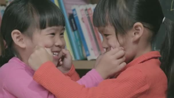 Азиатские сестры касаются щек друг друга и улыбаются лицом к лицу. две милые маленькие девочки играют вместе дома. Любимая семья проводит время вместе в помещении. - Кадры, видео