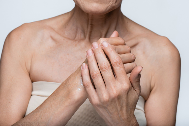 visão parcial da mulher de meia idade aplicando creme na mão isolado em cinza  - Foto, Imagem