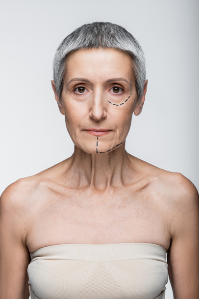 mature woman with wrinkles and marked lines on face looking at camera isolated on grey  - Photo, Image