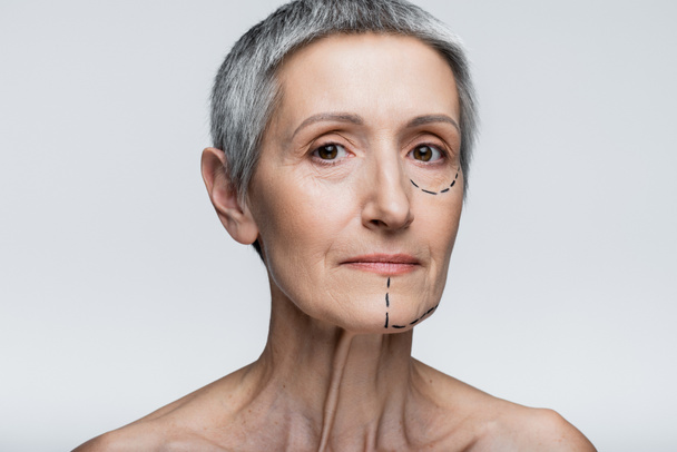 mature woman with marked lines on face looking at camera isolated on grey  - Foto, Imagem