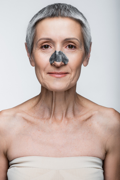 χαμογελαστή ώριμη γυναίκα με μαύρο μπάλωμα στη μύτη απομονωμένη σε γκρι  - Φωτογραφία, εικόνα