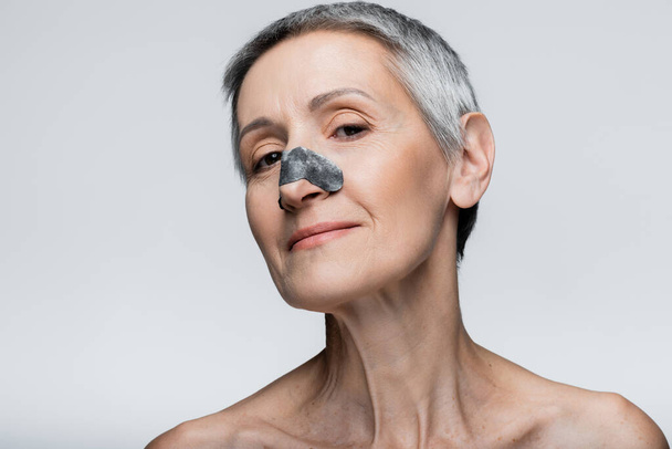 mujer alegre y madura con parche negro en la nariz aislado en gris  - Foto, Imagen