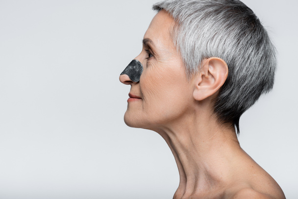 vue latérale de la femme souriante et mature avec tache noire sur le nez isolé sur gris  - Photo, image