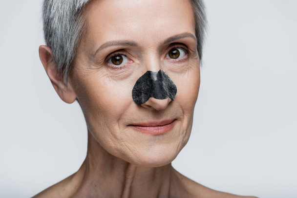 κοντινό πλάνο ευτυχισμένης μεσήλικας γυναίκας με μαύρο μπάλωμα στη μύτη απομονωμένη σε γκρι  - Φωτογραφία, εικόνα