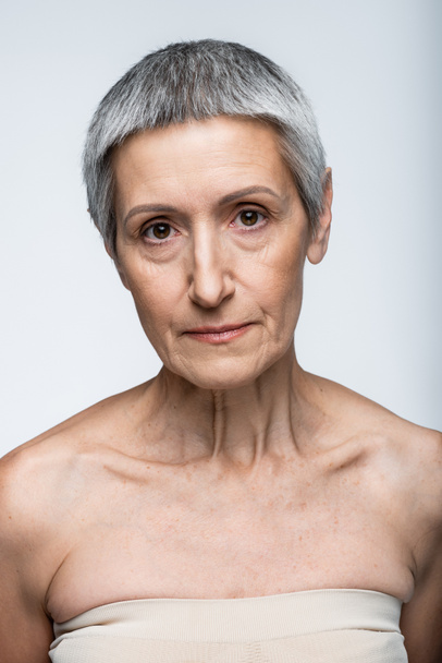 volwassen vrouw met blote schouders en rimpels geïsoleerd op grijs - Foto, afbeelding