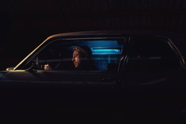 Людина з світлим волоссям вночі сидить у американській класичній м "язовій машині.. - Фото, зображення