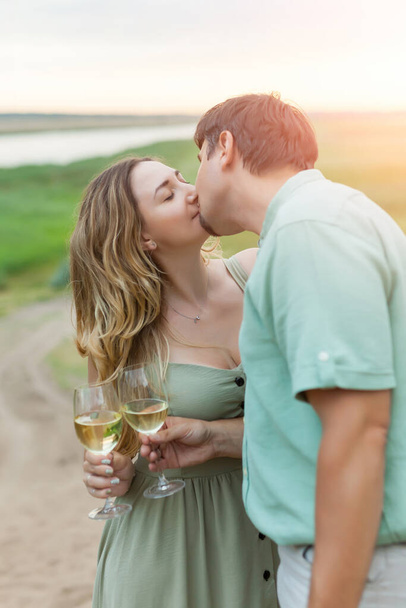 Romantic couple toasting wine glasses outdoors. Beautiful woman clinking wine glass with her man and kissing. - Fotografie, Obrázek