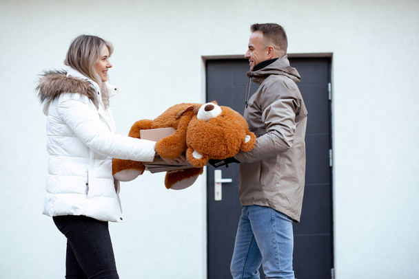 Portrait of happy smiling cute couple in casual upper garments stand holding huge orange teddy bear and paperboard box. - Photo, image